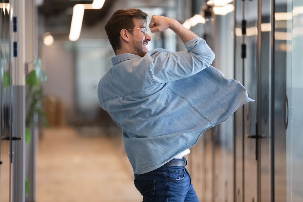 Funny businessman dancing in empty modern office hallway, showing yes gesture, excited employee in glasses celebrating success, promotion, moving in victory dance, rejoicing good work results