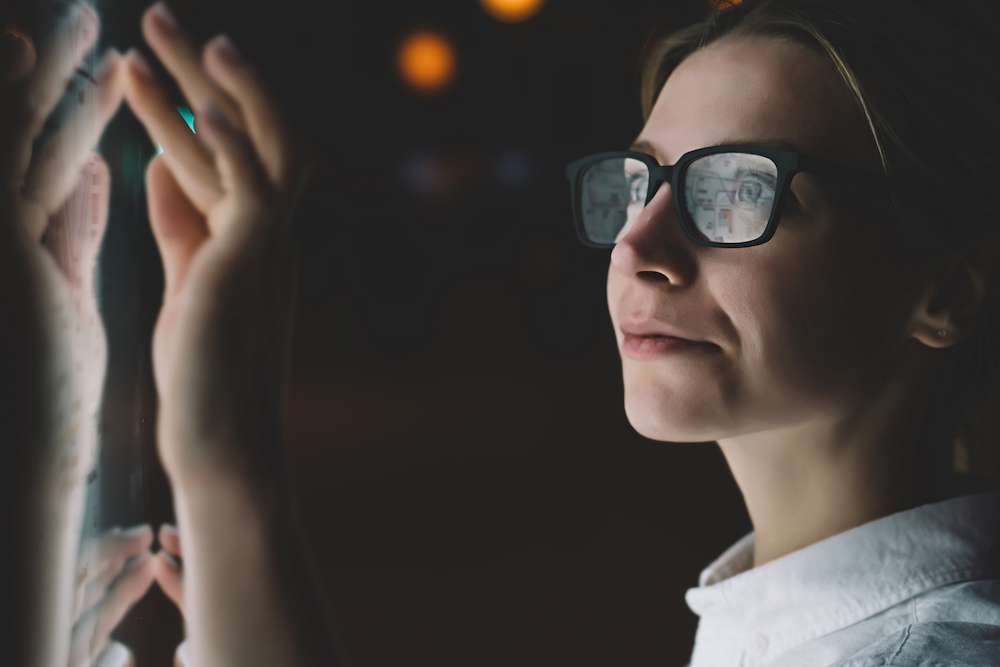 Female standing at display with advanced innovative technology. Young woman touching with finger sensitive screen while selecting surface option. Interactive kiosks with night light reflected on face